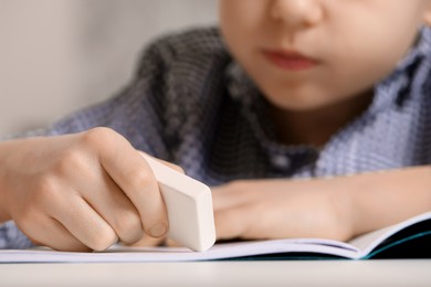 Little boy erasing mistake in his notebook at white desk, closeup
