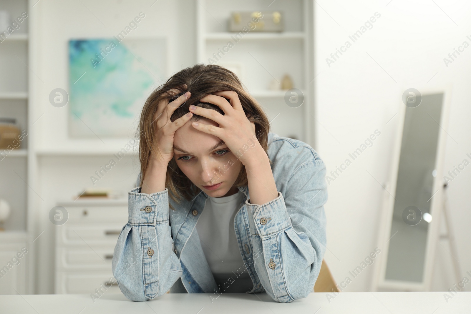 Photo of Sad young woman sitting at white table in room