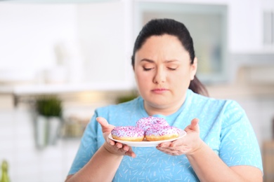 Sad overweight woman with donuts in kitchen. Failed diet