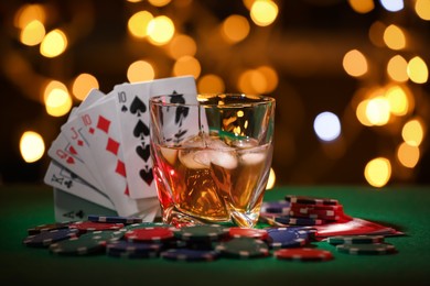 Photo of Casino chips, cards and alcohol drink on green table against blurred lights. Straight poker combination