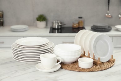 Photo of Clean plates, bowls and cup on white marble table in kitchen