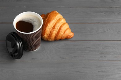 Photo of Coffee to go. Paper cup with tasty drink and croissant on grey wooden table. Space for text