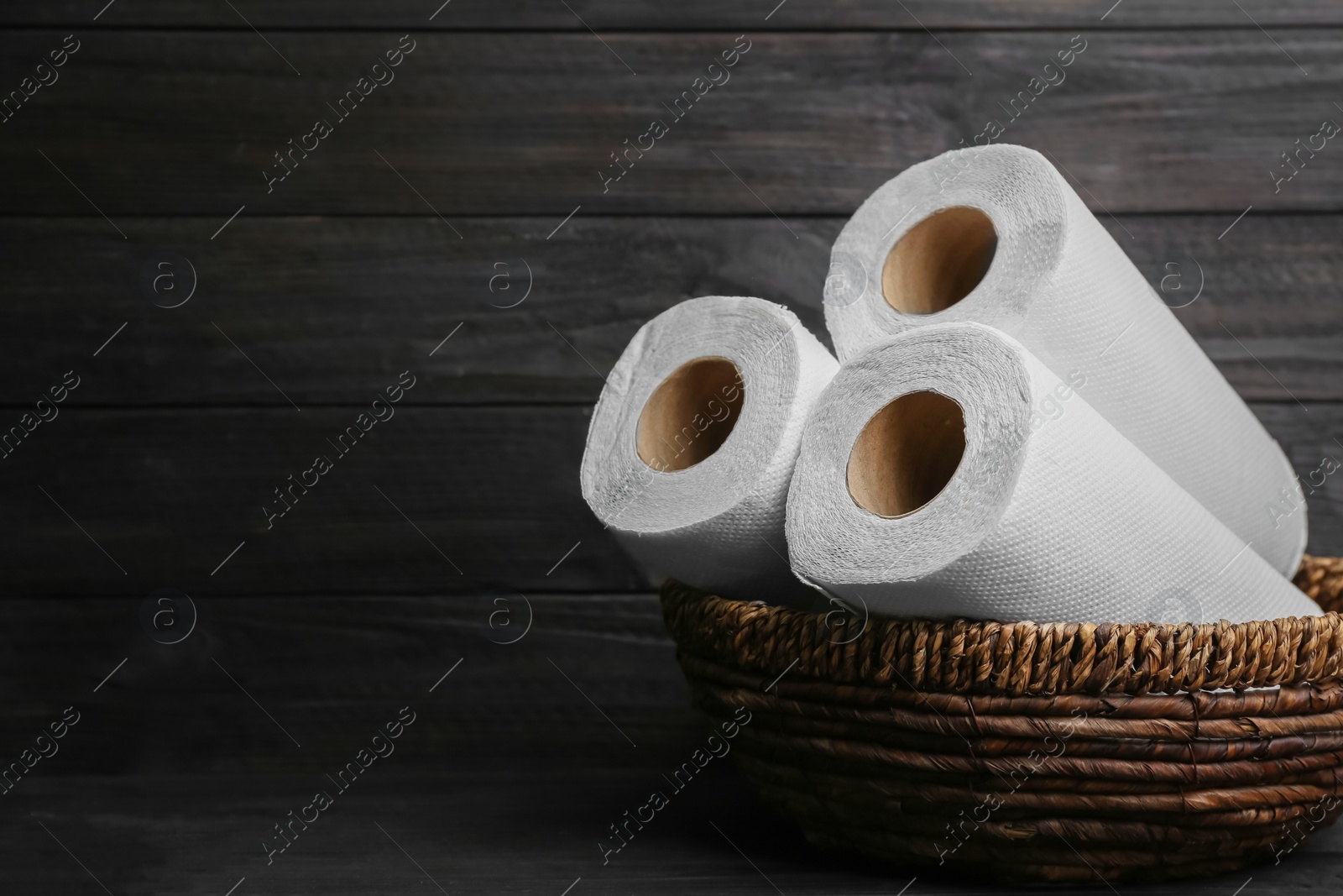 Photo of Rolls of paper towels in wicker basket on wooden table, space for text