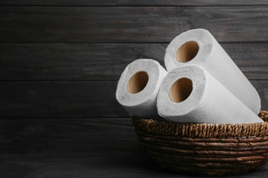 Photo of Rolls of paper towels in wicker basket on wooden table, space for text