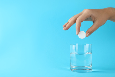 Photo of Woman putting tablet into glass of water on light blue background, space for text