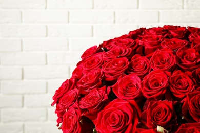 Photo of Luxury bouquet of fresh red roses near white brick wall, closeup