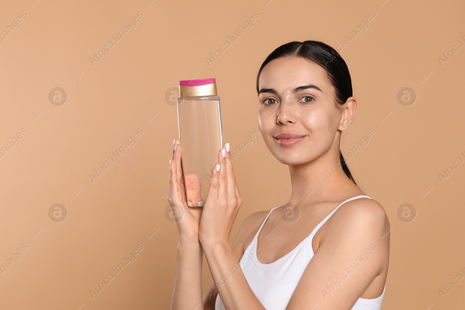 Photo of Young woman with bottle of micellar water on beige background, space for text