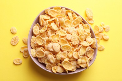 Photo of Bowl of tasty crispy corn flakes on pale yellow background, flat lay
