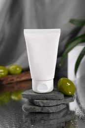 Photo of Tube of natural cream and olive on wet table