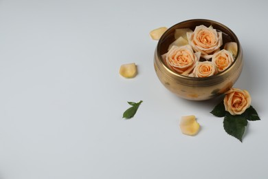 Photo of Tibetan singing bowl with water and beautiful rose flowers on white background, space for text