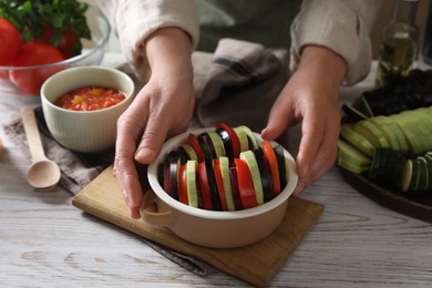 Cooking delicious ratatouille. Woman holding bowl with fresh cut vegetables at white wooden table, closeup