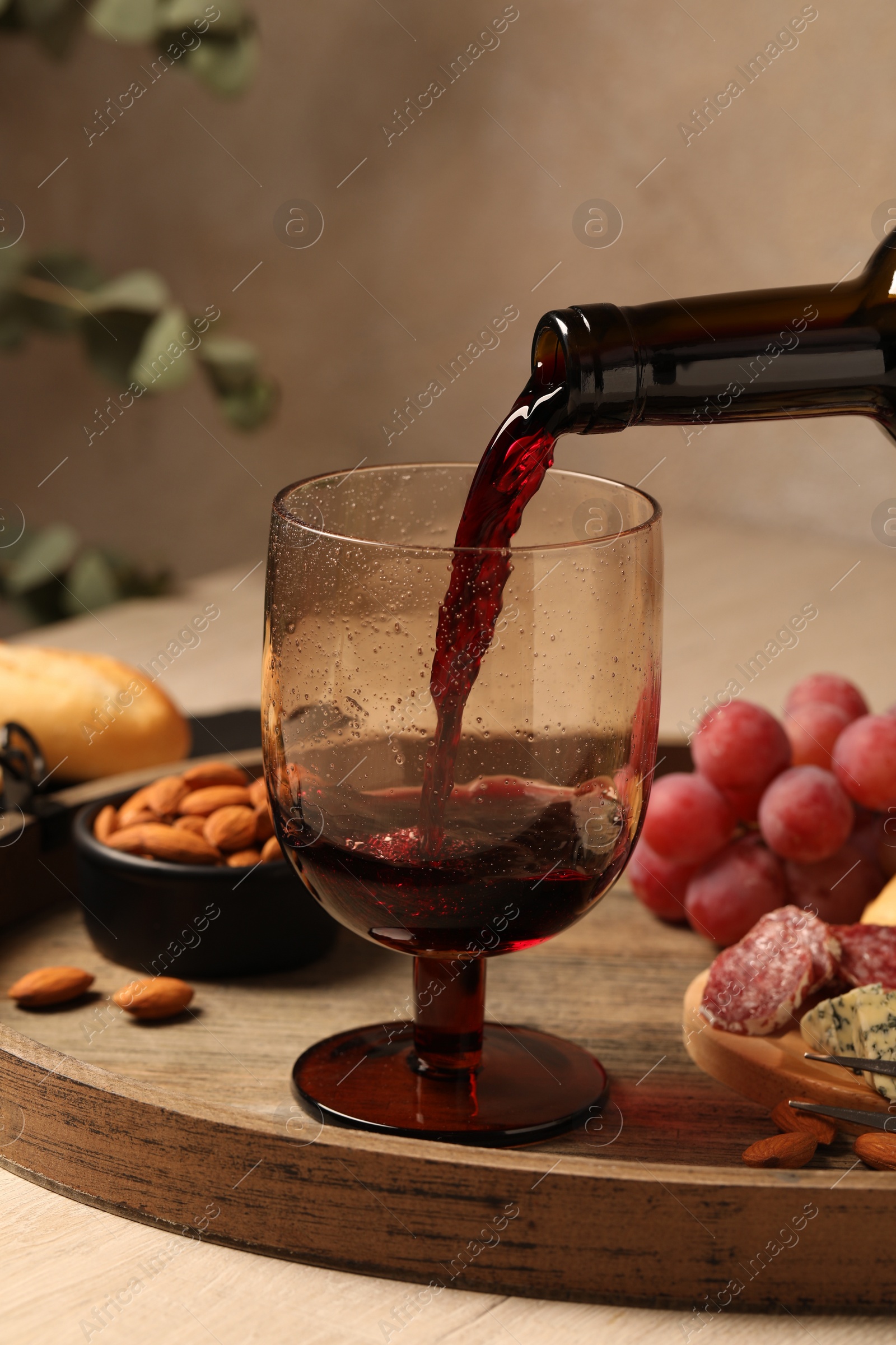 Photo of Pouring red wine into glass at wooden table, closeup