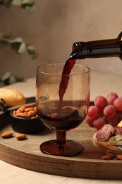 Photo of Pouring red wine into glass at wooden table, closeup