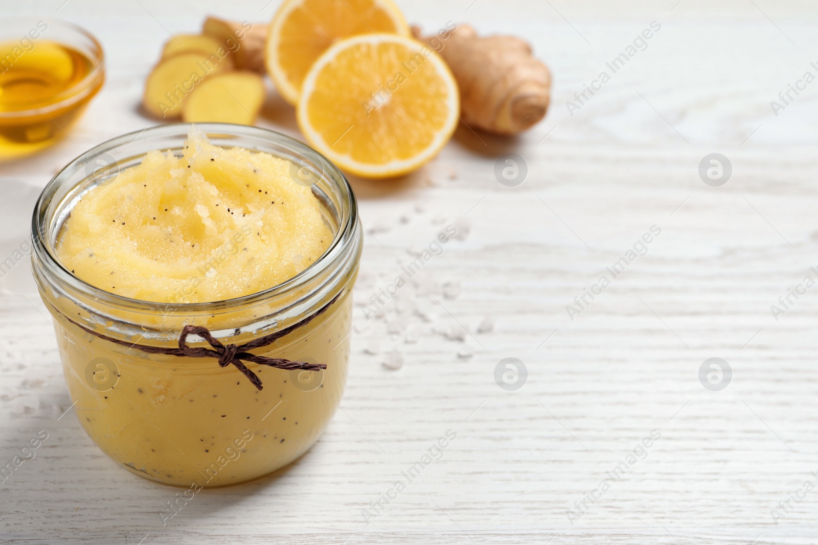 Photo of Body scrub in glass jar on white wooden table, space for text