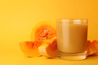 Tasty pumpkin juice in glass and cut pumpkin on orange background