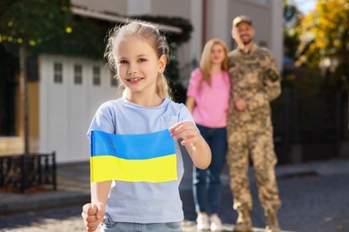 Photo of Child with Ukrainian flag, her father in military uniform and mother on city street, space for text. Family reunion