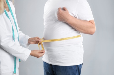 Photo of Doctor measuring senior man's waist on grey background. Weight loss