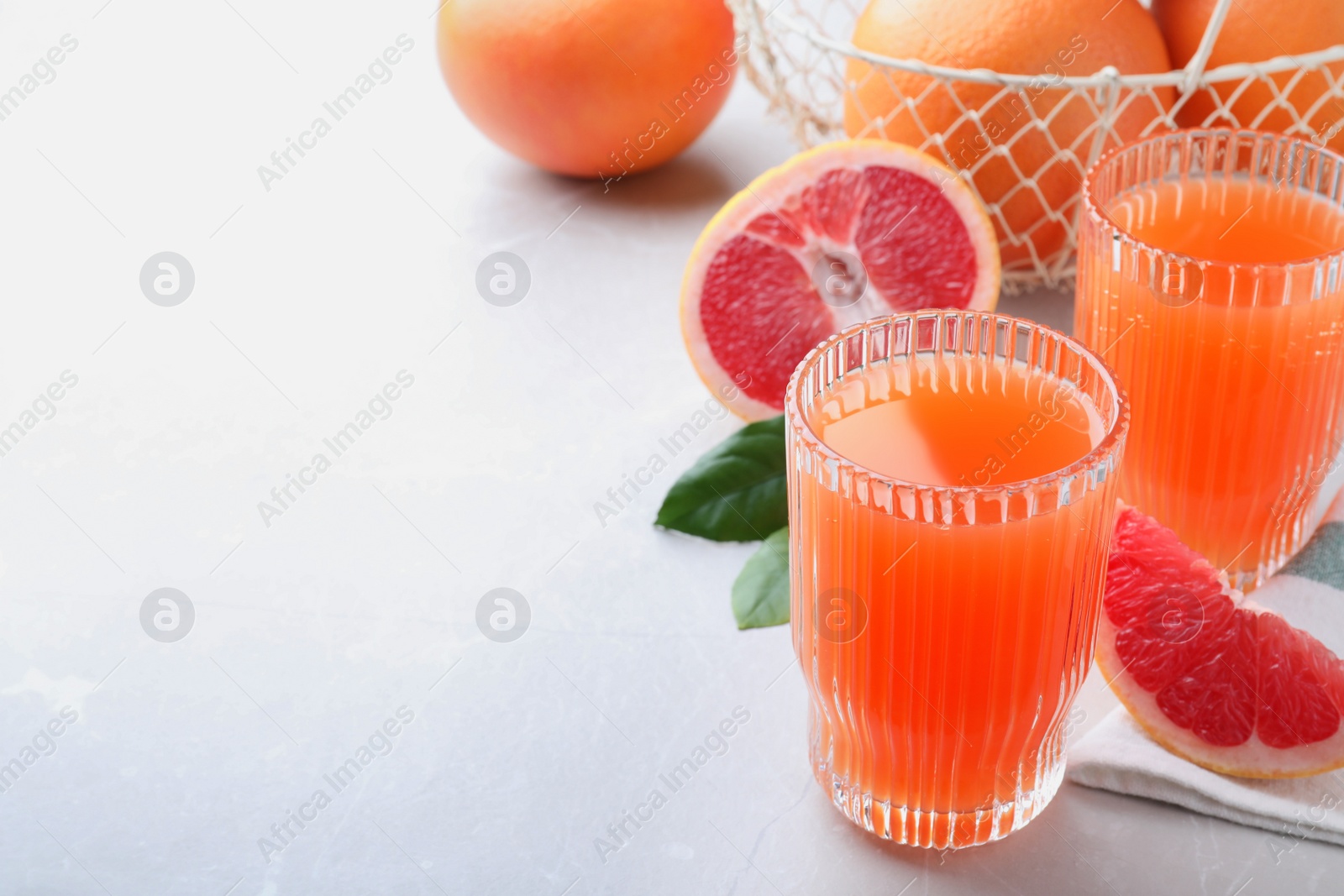 Photo of Tasty freshly made grapefruit juice and fruit on light grey marble table. Space for text