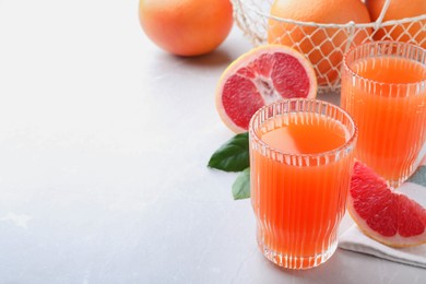 Photo of Tasty freshly made grapefruit juice and fruit on light grey marble table. Space for text