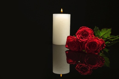 Photo of Beautiful red roses and candle on black background. Funeral symbol
