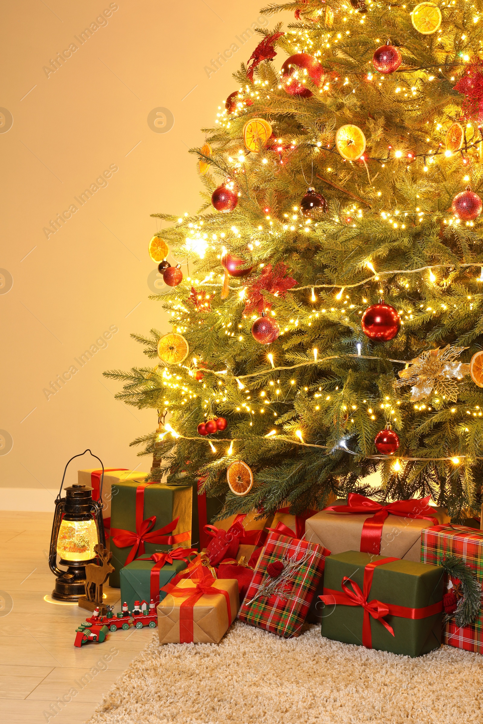 Photo of Many gift boxes under Christmas tree decorated with ornaments and festive lights in room