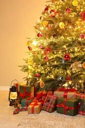 Many gift boxes under Christmas tree decorated with ornaments and festive lights in room