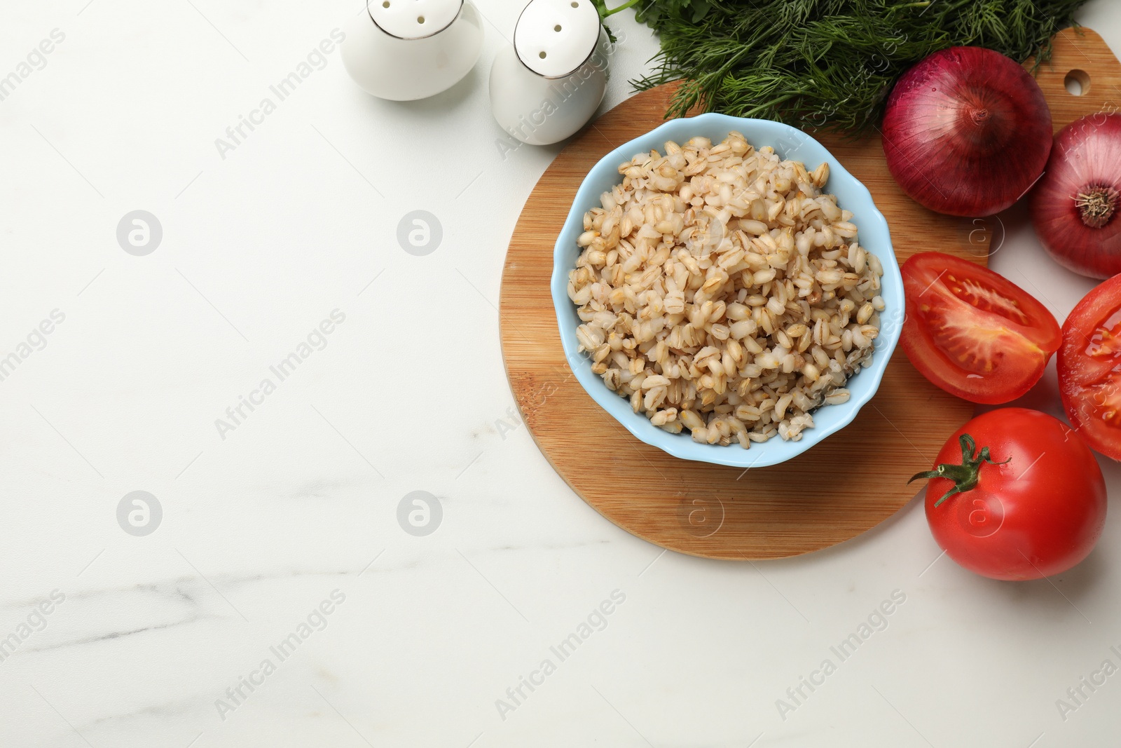 Photo of Delicious pearl barley in bowl served on white marble table, top view. Space for text