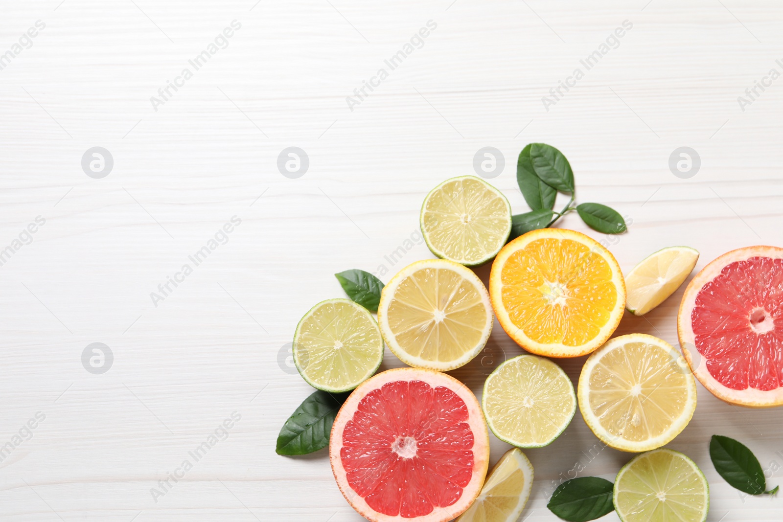 Photo of Different cut citrus fruits and leaves on white wooden table, flat lay. Space for text