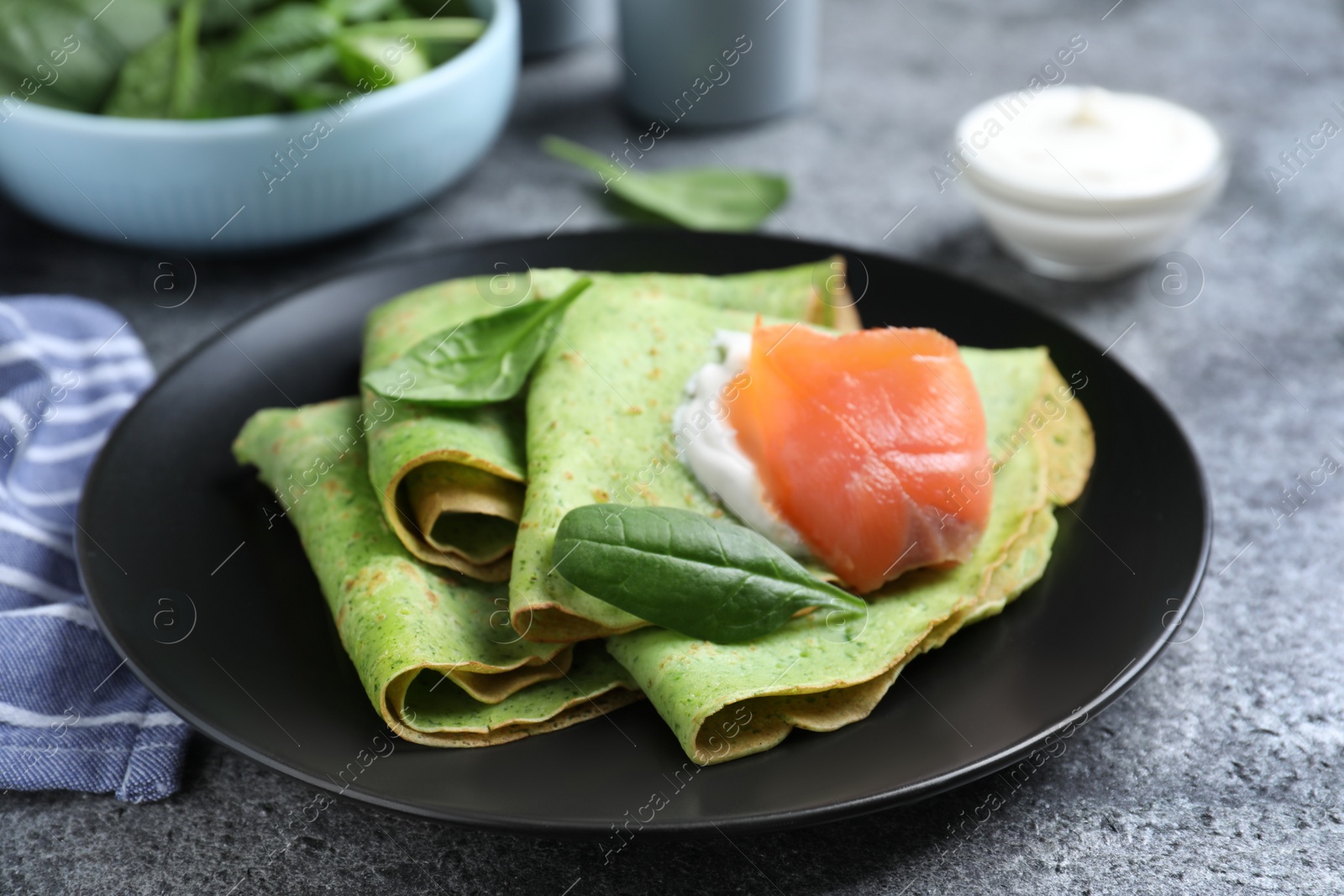 Photo of Delicious spinach crepes with salmon and cream on grey table