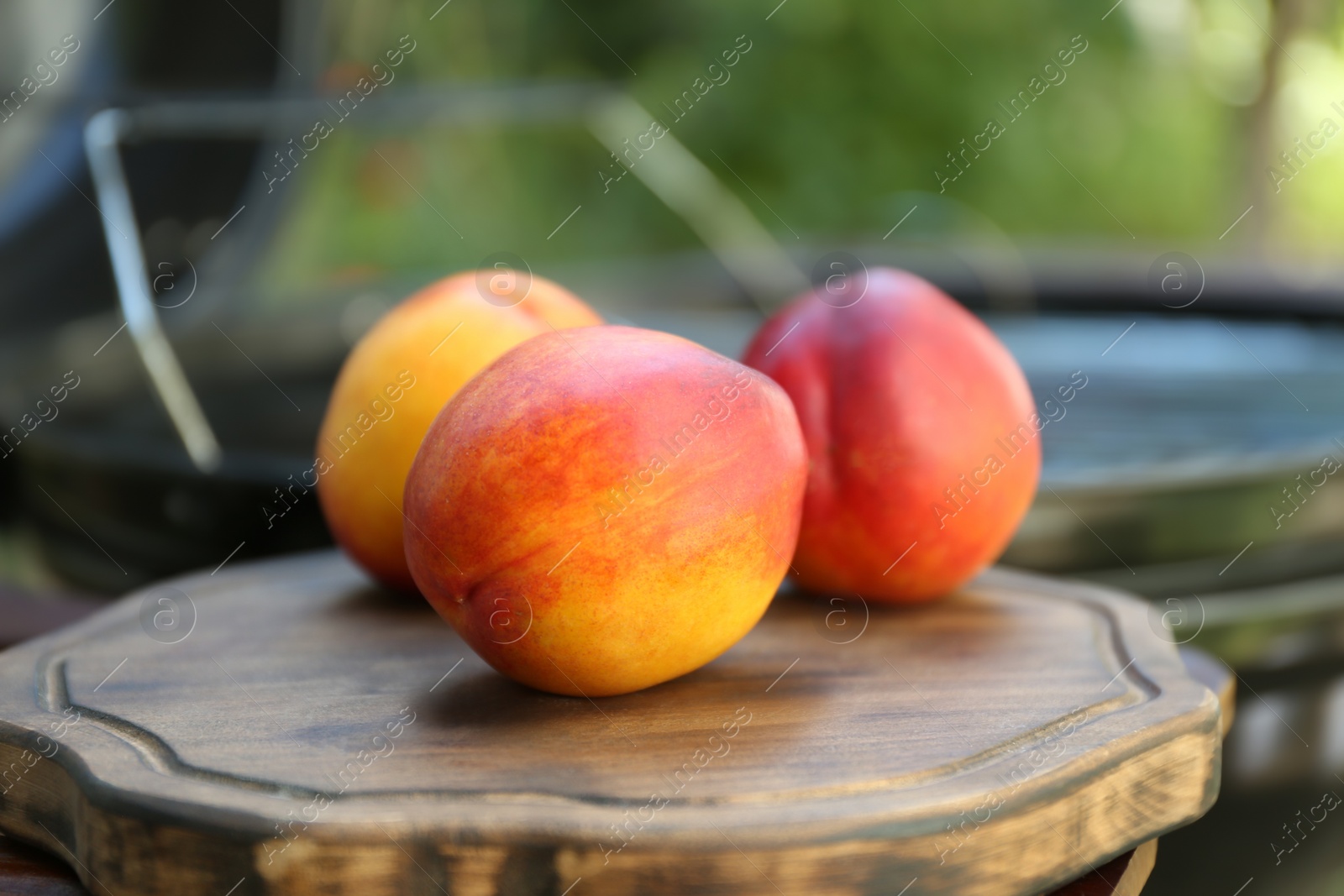 Photo of Fresh peaches on wooden board near modern grill outdoors, closeup