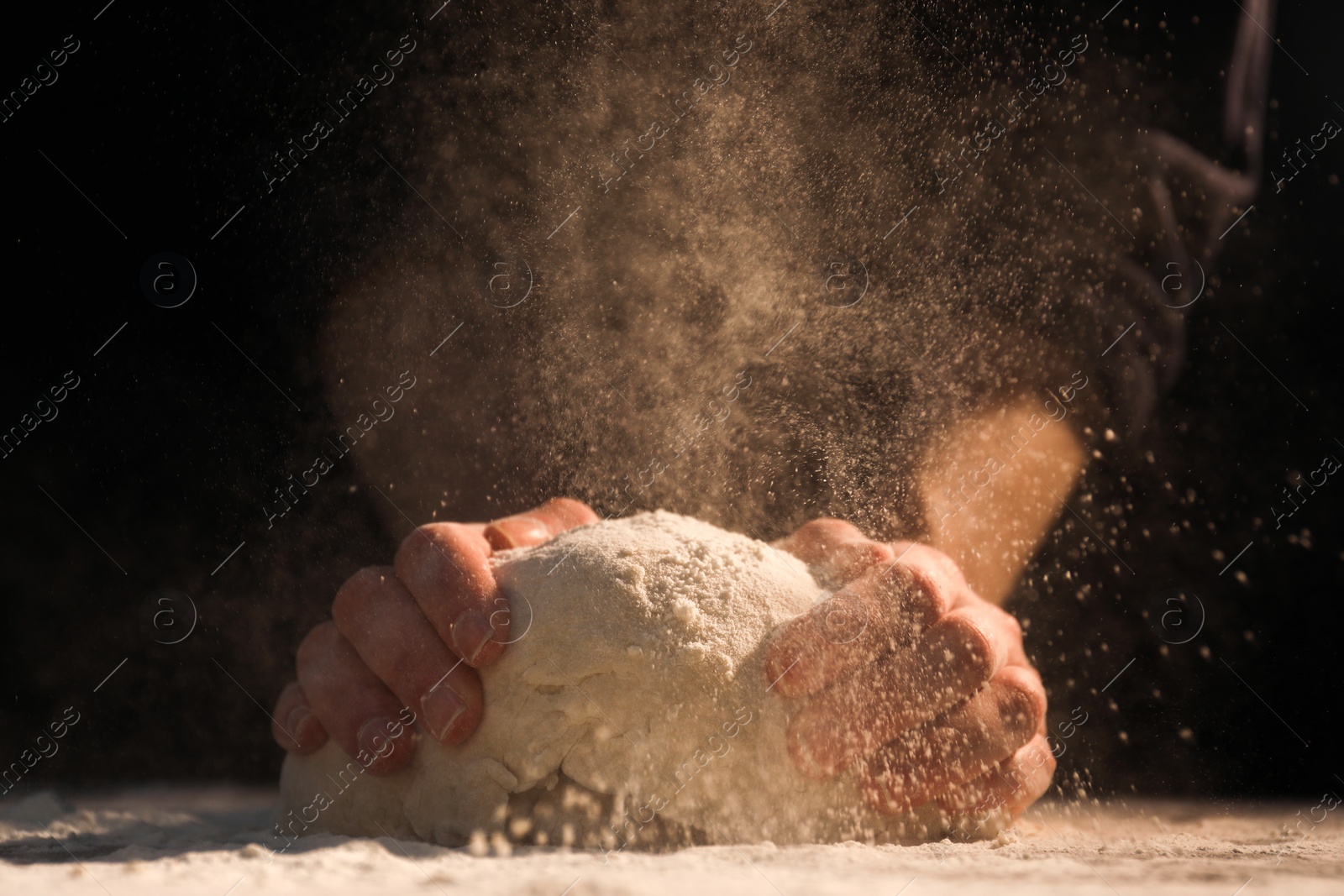 Photo of Making bread. Woman kneading dough at table on dark background, closeup