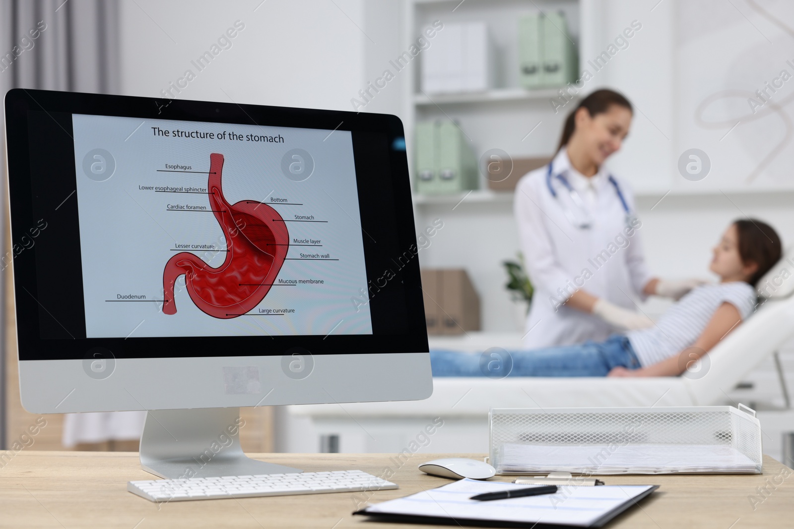 Photo of Gastroenterologist examining girl in clinic, focus on computer with image of stomach on table