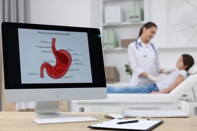 Gastroenterologist examining girl in clinic, focus on computer with image of stomach on table