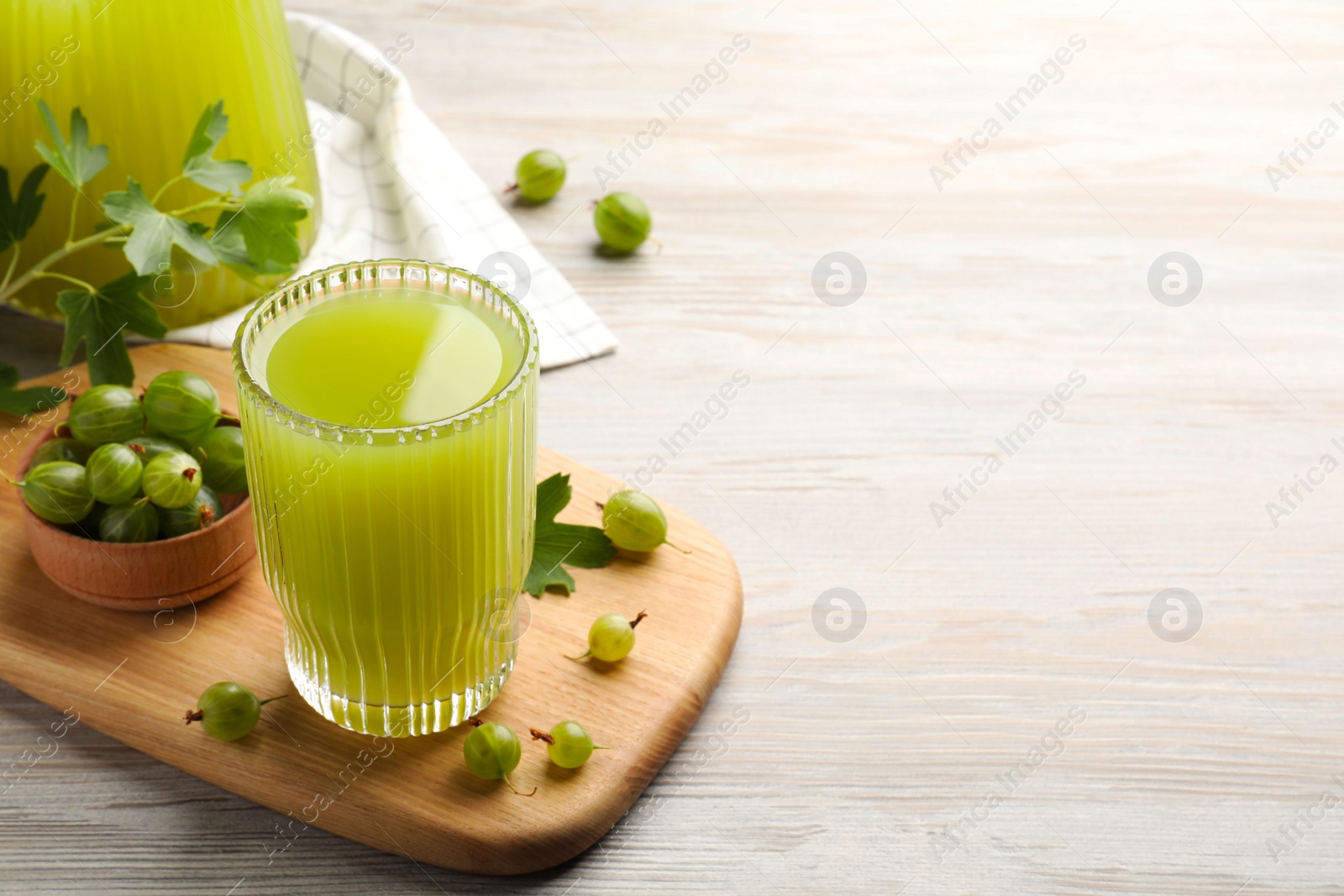 Photo of Tasty gooseberry juice and fresh berries on white wooden table. Space for text