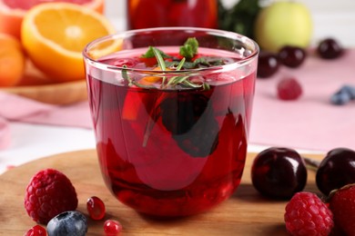 Photo of Glass of delicious sangria, fruits and berries on wooden board, closeup