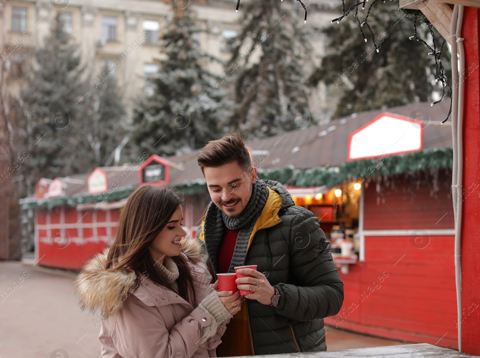 Photo of Young couple with cups of mulled wine at winter fair. Space for text