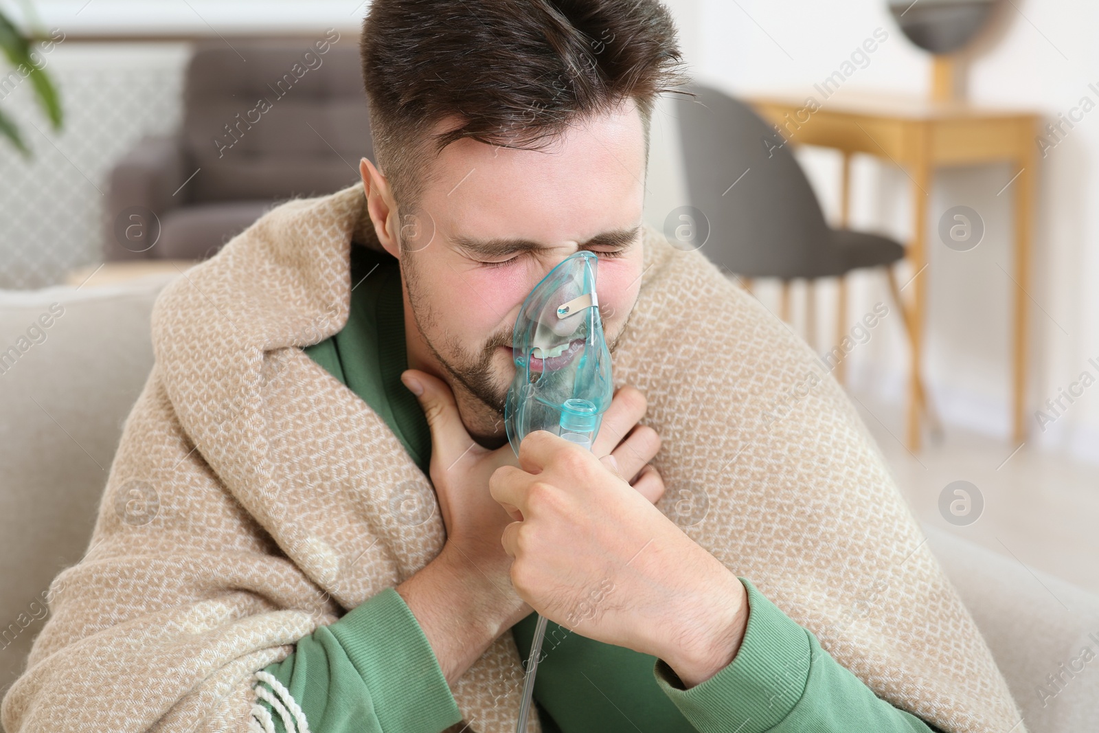 Photo of Sick man using nebulizer for inhalation indoors
