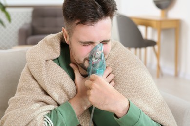 Photo of Sick man using nebulizer for inhalation indoors