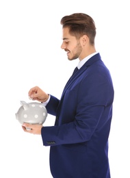 Young businessman putting money into piggy bank on white background