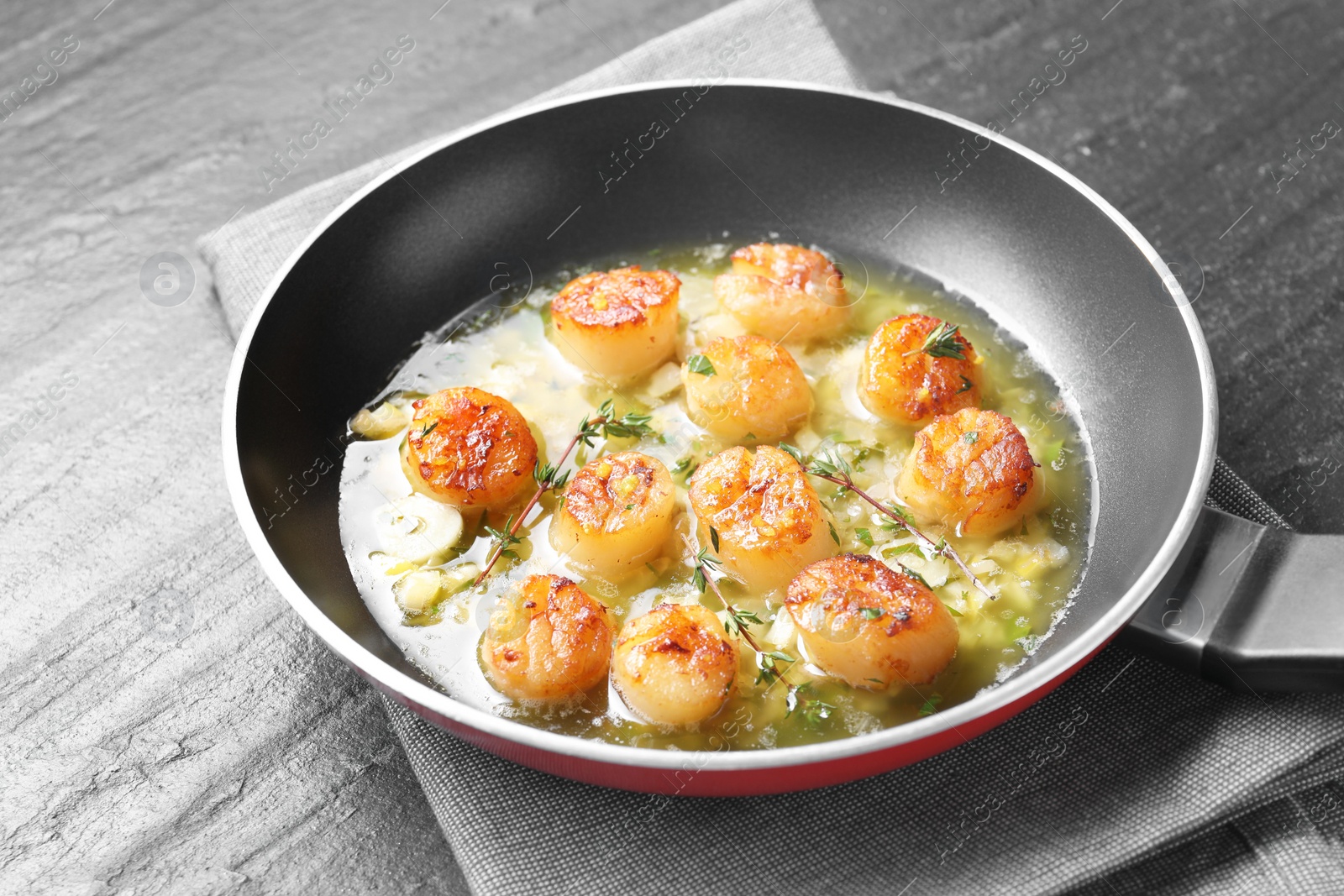 Photo of Delicious scallops with sauce in frying pan on dark gray textured table, closeup