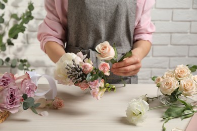 Photo of Florist creating beautiful bouquet at white table indoors, closeup