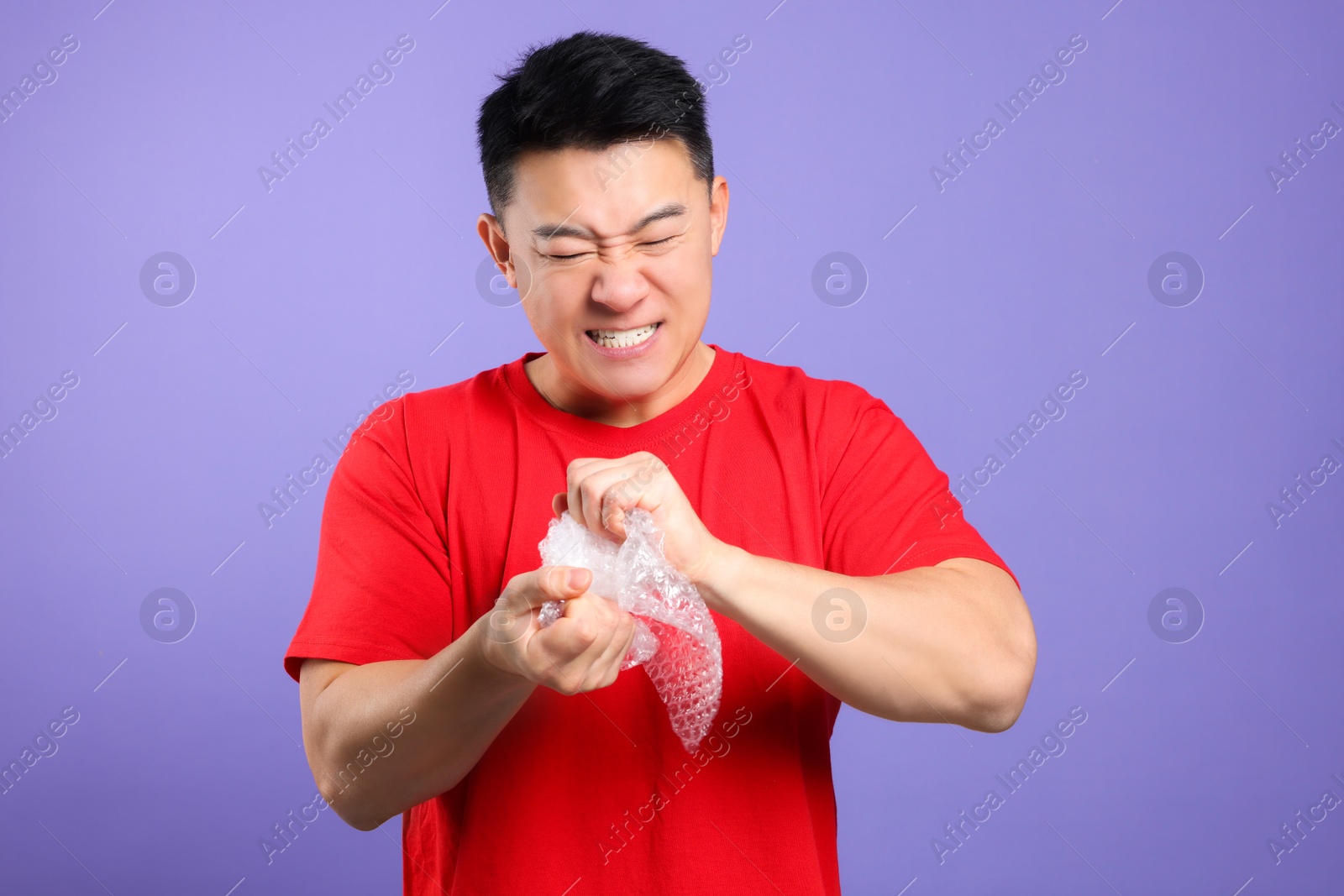 Photo of Emotional asian man with bubble wrap on purple background