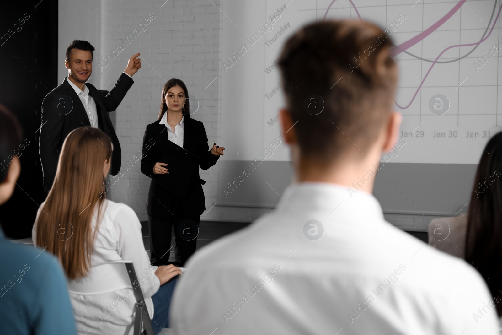 Photo of Business trainers giving lecture in conference room with projection screen