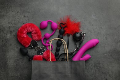 Photo of Paper shopping bag with different sex toys on grey table, flat lay