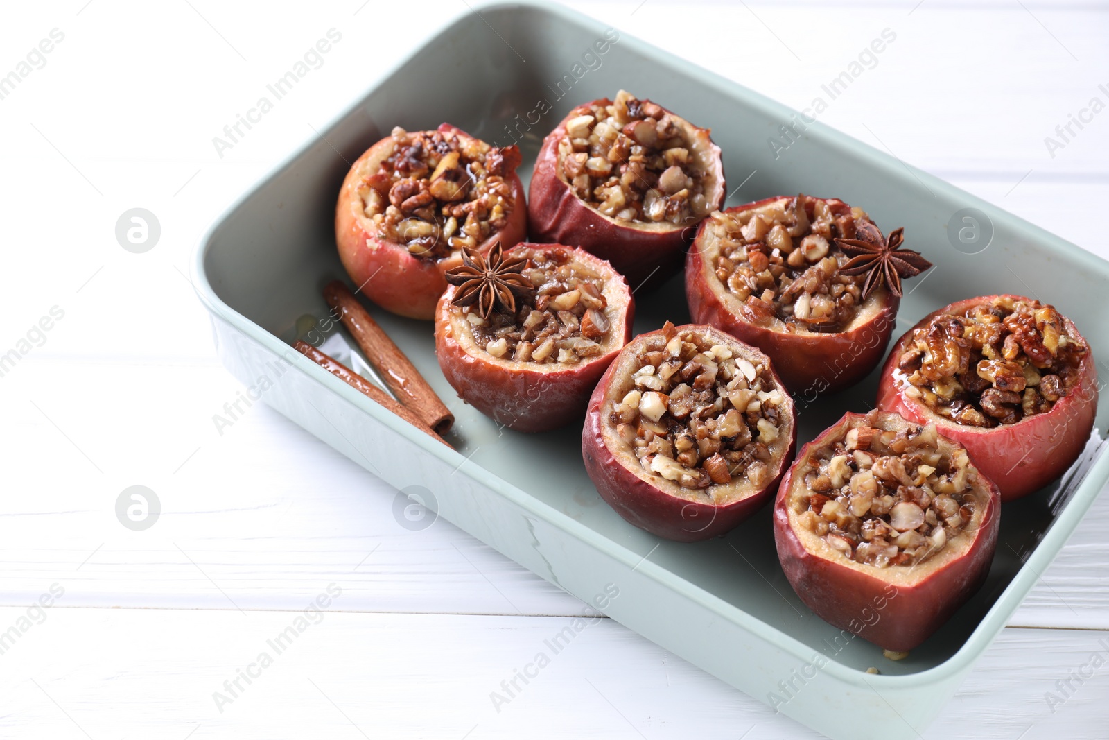 Photo of Tasty baked apples with nuts, honey and spices in dish on white wooden table, closeup