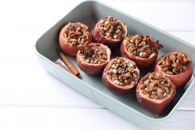 Tasty baked apples with nuts, honey and spices in dish on white wooden table, closeup