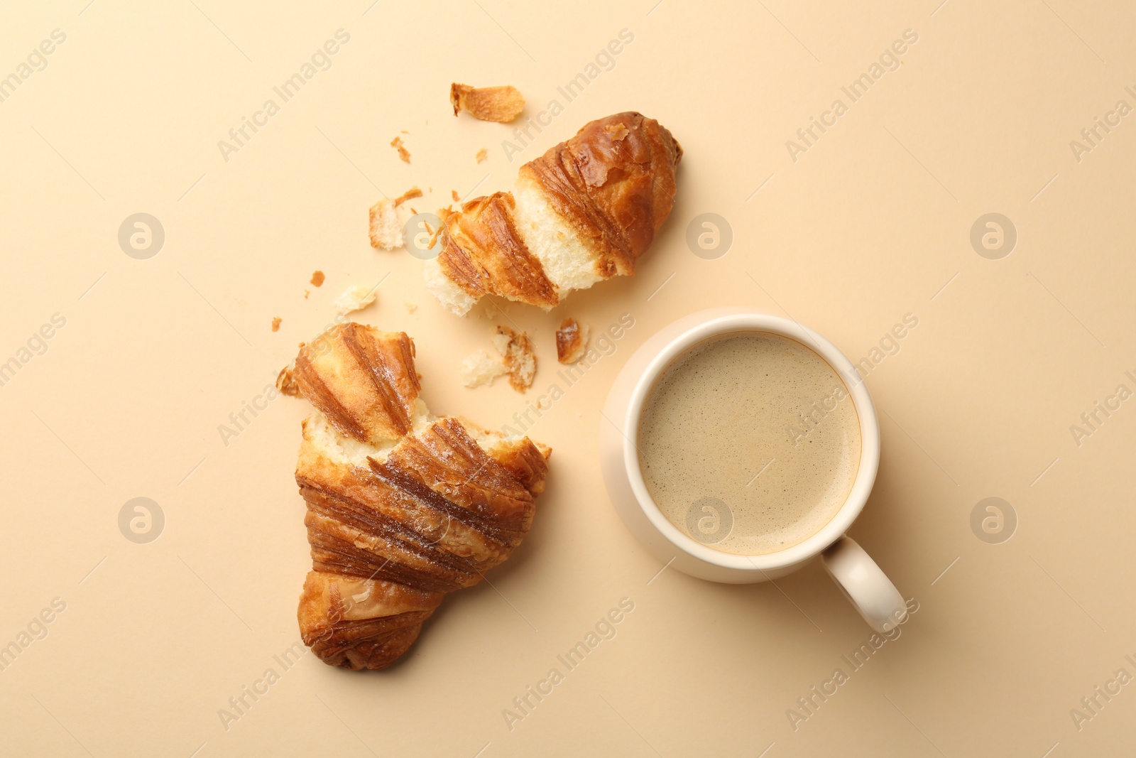 Photo of Delicious croissant and cup of coffee on beige table, flat lay