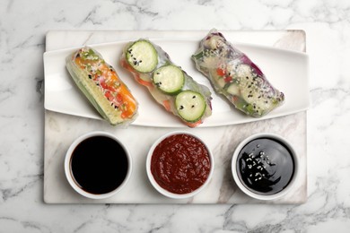 Photo of Different delicious rolls wrapped in rice paper on white marble table, top view