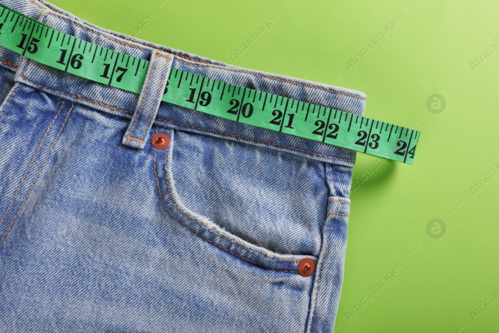 Photo of Jeans and measuring tape on light green background, top view. Weight loss concept