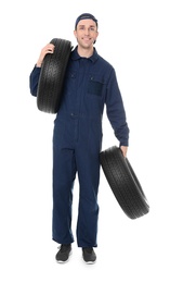 Young mechanic in uniform holding car tires on white background